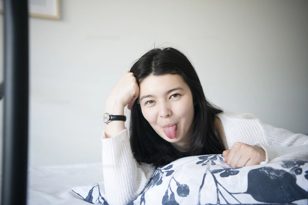 ベッドに寝転んでスマホを触っている女性の写真素材 [FYI02840086