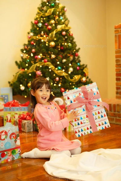 クリスマスツリーの前でプレゼントを抱える女の子の写真素材 