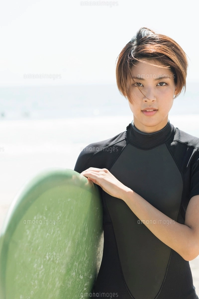 サーフボードを持つウェットスーツを着た20代女性の写真素材 