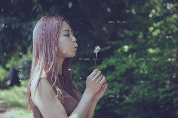 たんぽぽの綿毛を吹く美しい女性のポートレートの写真素材 