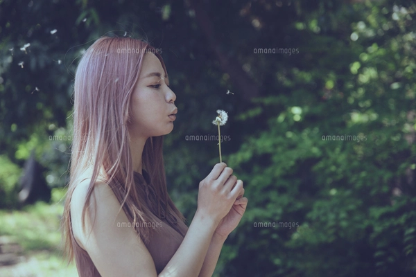たんぽぽの綿毛を吹く美しい女性のポートレートの写真素材 